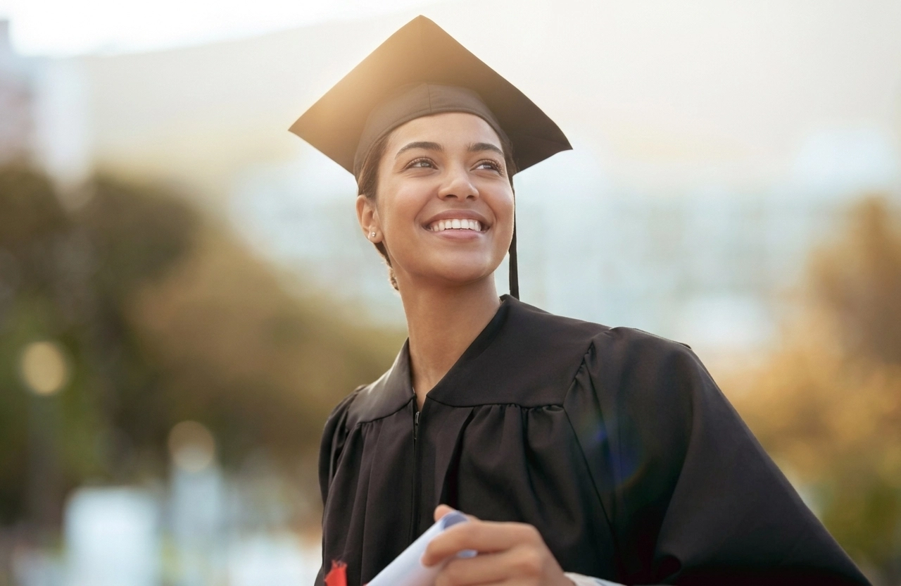 Aluna com traje de formatura olha para o horizonte e sorri